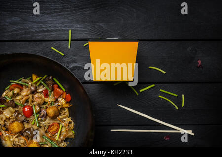 Faire sauter les nouilles Udon avec des fruits de mer et légumes en wok casserole sur fond de bois noir. avec une boîte de nouilles. vue d'en haut. Banque D'Images