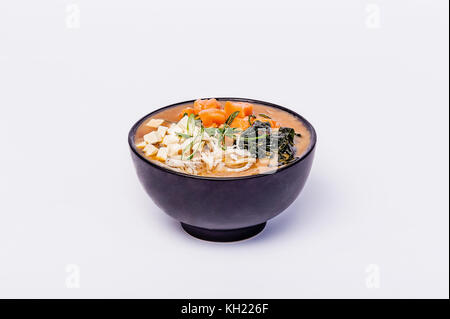 La soupe miso japonaise avec le tofu et le saumon dans un bol noir sur fond blanc. Banque D'Images