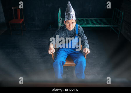 L'homme effrayé dans du papier aluminium hat se trouve en chaise Banque D'Images