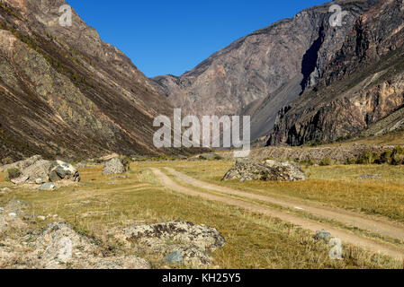 Vue panoramique sur la route de gravier avec des pierres et de la végétation le long des routes, en passant par la vallée entre les rochers sur le fond bleu du ciel Banque D'Images