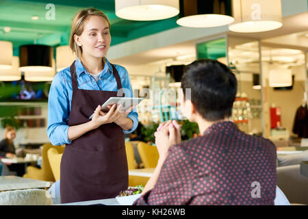 Portrait of smiling young waitress à partir du client dans cafe using digital tablet, copy space Banque D'Images