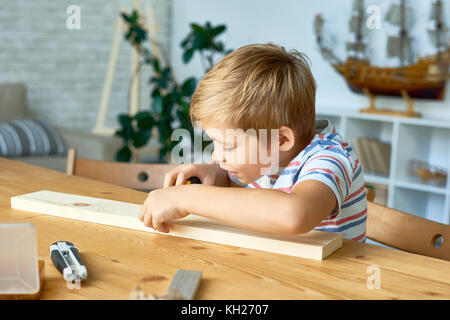 Portrait of cute little boy travail du bois assis à table haute et souriant, ce modèle en bois Banque D'Images