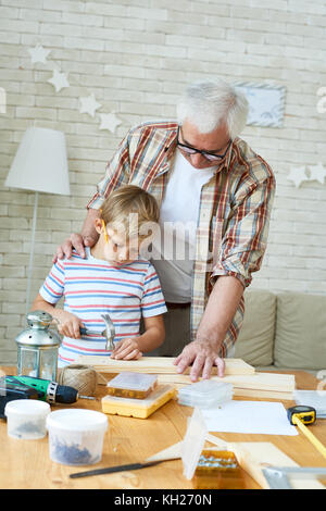 Portrait of senior man helping little boy marteler les ongles tout en maquette en bois ensemble à la maison Banque D'Images