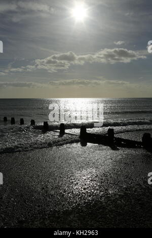 Bognor Regis. Le soleil se reflète au large de la mer sur une plage déserte de la côte sud du Royaume-Uni. Mer calme, marée basse. Montre des brise-lames en bois pour empêcher l'érosion côtière. Banque D'Images