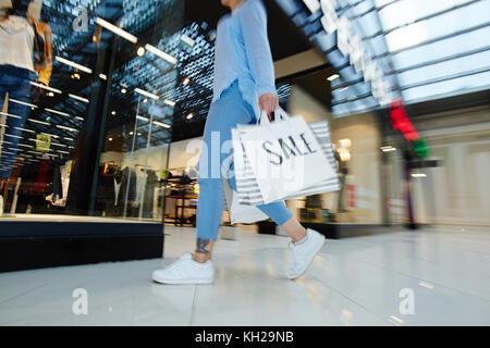 Se dépêchant shopper avec paperbags en marchant le long de la fenêtre afficher en grand centre commercial au cours de vente Banque D'Images