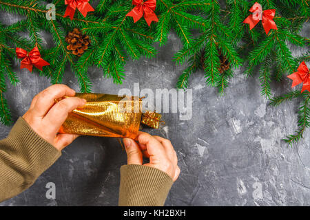 Branches de sapin avec les cônes et arcs rouge sur un fond de béton gris. nouvelle année Noël. les mains avec un sac de cadeaux Banque D'Images