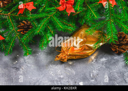 Branches de sapin avec les cônes et arcs rouge sur un fond de béton gris. nouvelle année. Noël sac d'or avec des cadeaux Banque D'Images