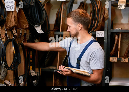 Vue de côté portrait de jeune mécanicien contrôle de stock tout en faisant l'inventaire en magasin outils industriels Banque D'Images