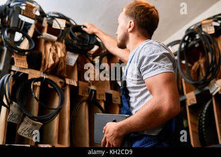 Low angle portrait de jeune mécanicien contrôle de stock tout en faisant l'inventaire en magasin outils industriels Banque D'Images