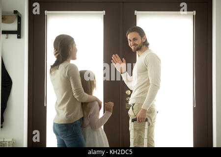 Mère et fille voir le père de partir pour un voyage, maman avec kid girl de dire au revoir à papa en agitant la main à la maison debout tenant la porte de tra Banque D'Images