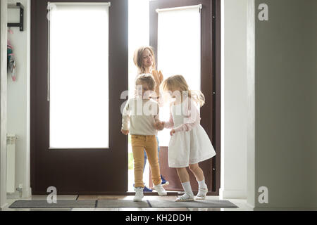 Heureux jeune mère avec son fils et sa fille de l'ouverture de la porte à la maison de la galerie marchande, seule la maman et les petits enfants de retourner à la maison avec un sac en papier Banque D'Images