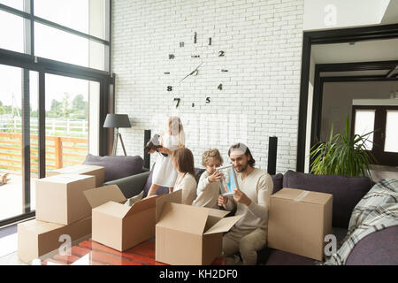 Les jeunes professionnels familles avec enfants unpacking boxes together sitting on sofa in modern living room de country house déménagement s'établir au nouveau domicile, les enfants hôtel Banque D'Images