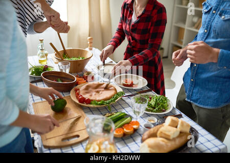 La section basse des gens méconnaissables et pie coupe légumes debout autour d'une table à manger avec des aliments Banque D'Images