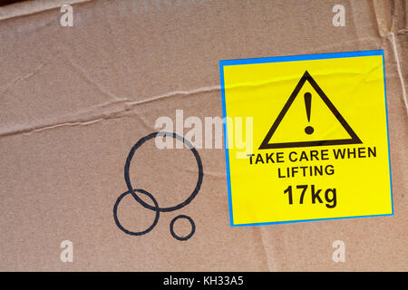 Prendre soin lors du levage de 17kg autocollant jaune étiquette collée sur carton fort Banque D'Images