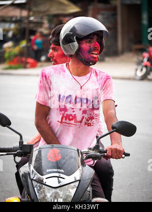 Les jeunes hommes népalais recouvert de poudre de couleur accueil retour sur un scooter après avoir célébré la fête hindoue Holi dans Pokhara, Népal Banque D'Images