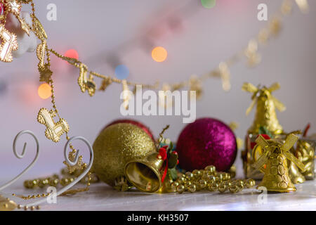 Décoration de Noël, cadeaux, des chaînes, des cloches et des boules colorées, réfléchissant sur le dessus d'une surface en bois blanc et fond blanc, avec l'arrière-plan flou Banque D'Images