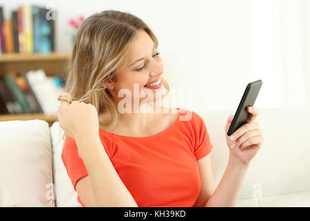 Femme franche et Flirter Datant en ligne avec un téléphone intelligent assis sur un canapé dans la salle de séjour à la maison Banque D'Images