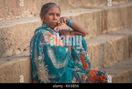 Femme âgée indienne avec une expression réfléchie assise sur l'escalier du ghat du Gange à Varanasi, Inde. Banque D'Images