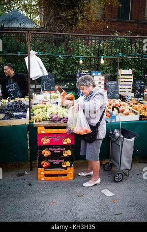 Une femme âgée qui fait ses courses dans un stand de fruits et légumes dans le marché du dimanche du petit village de Darnetal près de Rouen en France. Banque D'Images