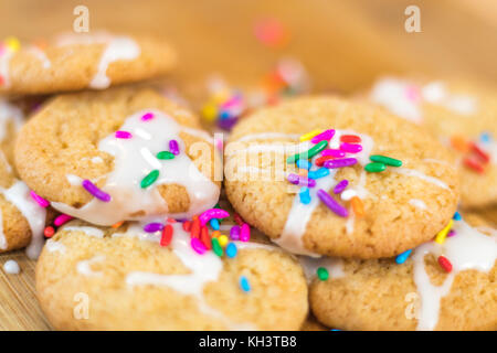 Sugar cookies fraîchement cuits avec glaçage blanc et couleur arc-en-ciel saupoudre sur planche de bois, selective focus Banque D'Images