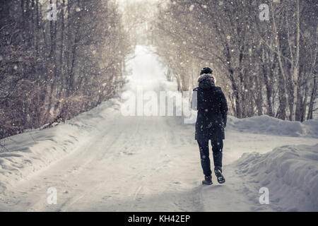 Lonely Woman walking on snowy winter road entre les arbres d'allée avec la lumière à la fin de la manière froide journée d'hiver de neige pendant with copy space Banque D'Images