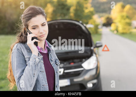 Jeune femme d'appeler un service d'assistance de voiture avec son smartphone, sa voiture est en panne Banque D'Images