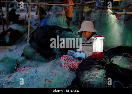 Mui Ne, le Viet Nam, groupe de travail personnes asiatiques sur la plage au petit matin, femme couture filet de pêche à la lumière de lampe, sur la mer vietnamiens Banque D'Images