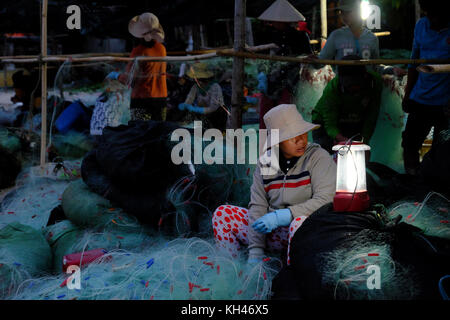 Mui Ne, le Viet Nam, groupe de travail personnes asiatiques sur la plage au petit matin, femme couture filet de pêche à la lumière de lampe, sur la mer vietnamiens Banque D'Images