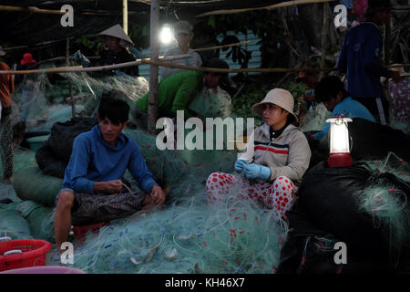 Mui Ne, le Viet Nam, groupe de travail personnes asiatiques sur la plage au petit matin, femme couture filet de pêche à la lumière de lampe, sur la mer vietnamiens Banque D'Images