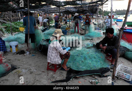 Mui Ne, le Viet Nam, groupe de travail personnes asiatiques sur la plage au petit matin, femme couture filet de pêche à la lumière de lampe, sur la mer vietnamiens Banque D'Images