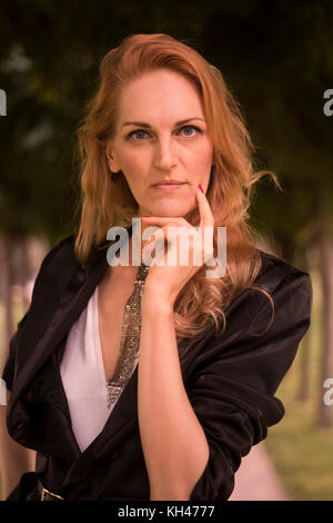 Une belle femme de race blanche à maturité, fin des années 40, à l'extérieur portrait haut du corps, la main sur le menton, looking at camera Banque D'Images