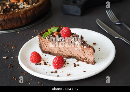 Gâteau au fromage au chocolat avec des framboises, des noix et de feuille de menthe sur plaque blanche. Vue rapprochée, selective focus Banque D'Images