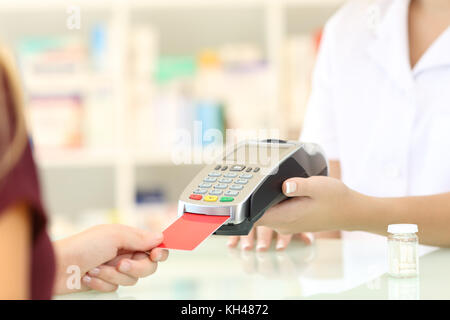 Près d'un pharmacien mains charge avec lecteur de carte de crédit sur un compteur dans une pharmacie Banque D'Images