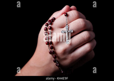 Femme priant mains tenant un rosaire avec Jésus Christ dans la croix ou crucifix sur fond noir. femme avec la foi chrétienne catholique Banque D'Images