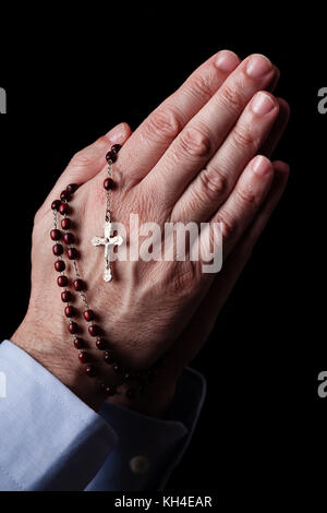 Priant mains tenant un rosaire avec Jésus Christ dans la croix ou crucifix sur fond noir. man avec la foi religieuse chrétienne catholique Banque D'Images