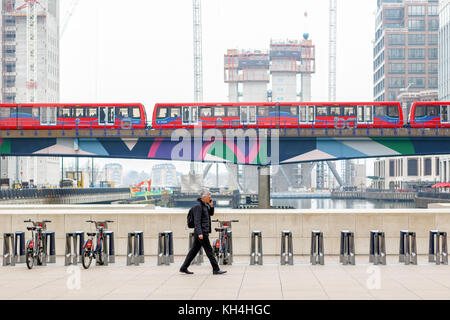 Londres, Royaume-Uni - 24 novembre 2017 - un homme marche sur Reuters plaza à canary wharf avec les trains dlr passant et chantier de construction à l'arrière-plan Banque D'Images