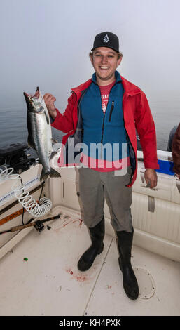 Jeune adulte en bateau de pêche, avec poisson de saumon pêché, matin brouillard dans le détroit de Johnstone au large de l'île de Vancouver, Colombie-Britannique, Canada Banque D'Images