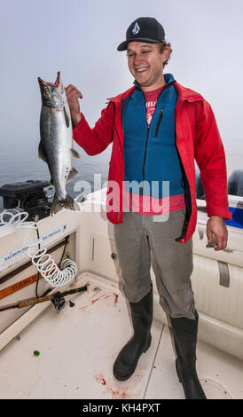 Jeune adulte en bateau de pêche, avec poisson de saumon pêché, matin brouillard dans le détroit de Johnstone au large de l'île de Vancouver, Colombie-Britannique, Canada Banque D'Images