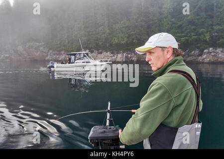 Adulte d'âge moyen avec pêche sur bateau, autre bateau passant, matin brouillard dans le détroit de Johnstone au large de l'île de Vancouver, Colombie-Britannique, Canada Banque D'Images