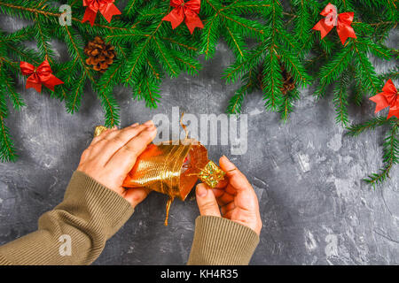 Branches de sapin avec les cônes et arcs rouge sur un fond de béton gris. nouvelle année Noël. les mains avec un sac de cadeaux Banque D'Images