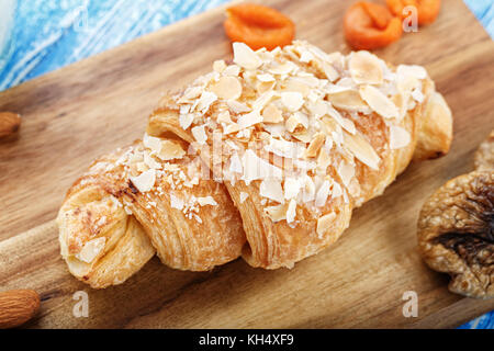 Fresh french croissant, parsemé de flocons d'amande, sur une planche en bois Banque D'Images