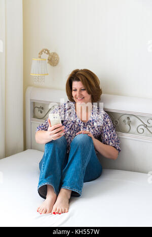 Smartphone bénéficie d'une femme assis sur le lit dans la chambre Banque D'Images