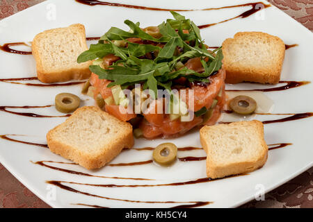 Tartare de saumon à l'avocat, le concombre, les olives et la roquette sur une plaque blanche avec des toasts et sauce balsamique. close-up. Banque D'Images