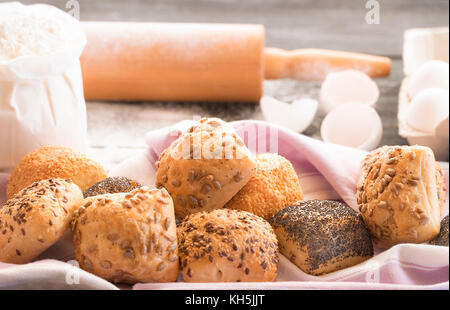 Close up image avec des petits pains fraîchement cuits, décoré de graines de pavot, de sésame, de lin et de tournesol, avec farine, oeufs et un rouleau à pâtisserie dans la zone Banque D'Images