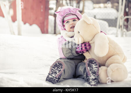 Faire place au beau bébé ours en peluche jouet assis sur la neige dans un parc à jour d'hiver ensoleillé froid pendant les vacances d'hiver Banque D'Images