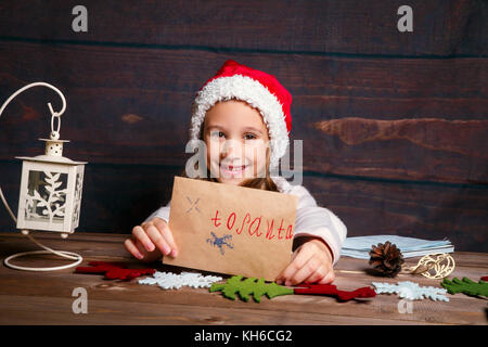 Enfant écrit une lettre au Père Noël . Funny Girl in Santa hat écrit lettre au Père Banque D'Images