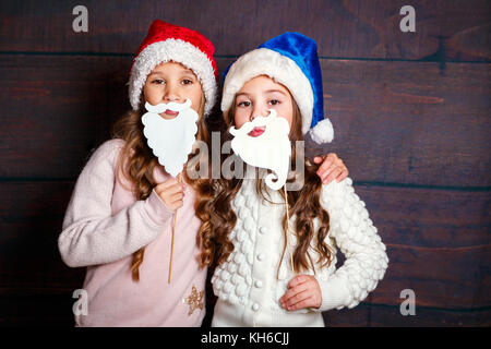Deux petites filles s'amuser .sourire concept de Noël. Smiling funny sisters in Santa hat sur fond de bois Banque D'Images