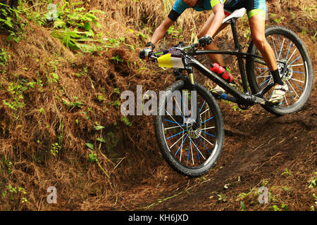 Un jeune cycliste féminine en descente sur une piste boueuse lors d'une course de vtt cross country dans la forêt Banque D'Images