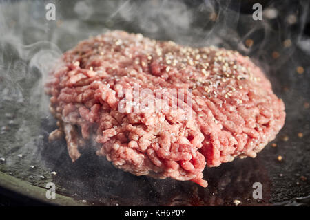 Un pâté d'hamburger sur un grill en fonte Banque D'Images