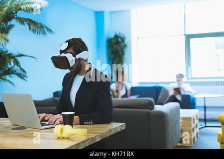 Male executive à l'aide de casque de réalité virtuelle alors que working on laptop in office Banque D'Images